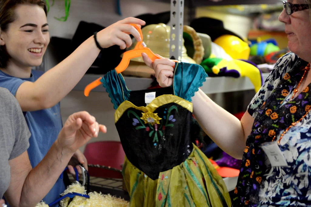 Therese hands volunteer Lily a Frozen costume for a client. Photo by Hurley Event Photography.