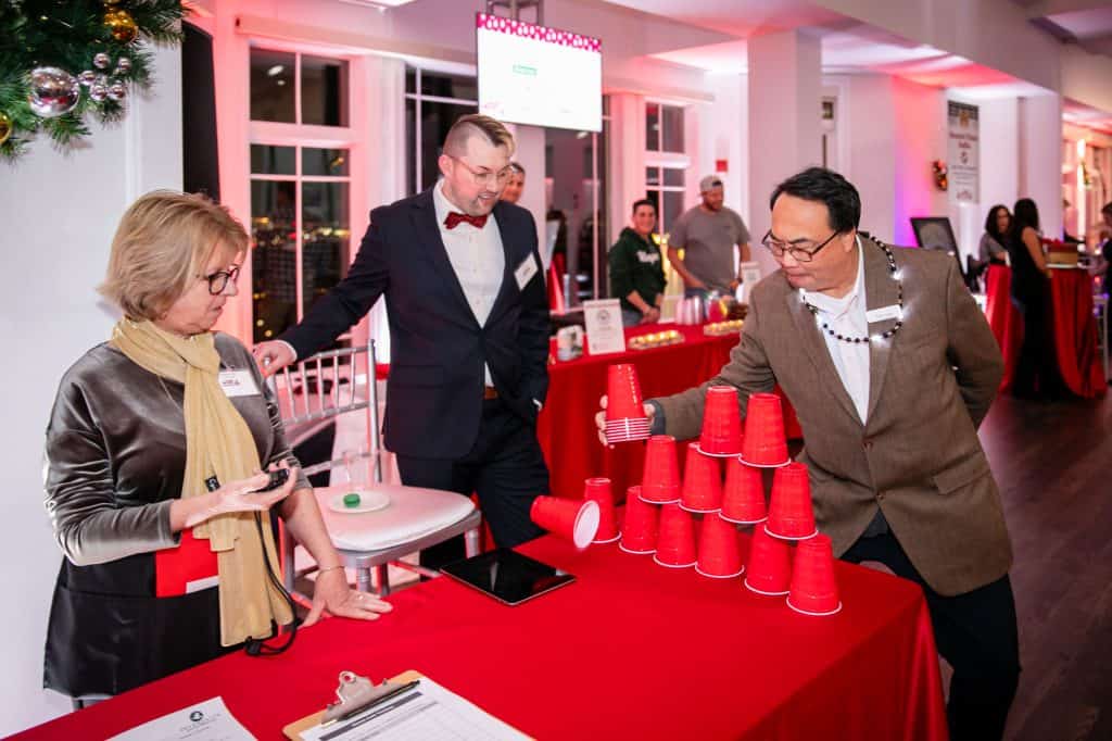 Interfaith volunteers Paula Cole, left, of Quincy, and James Madej, center, of Middleboro, ran the new Solo Cup Challenge game at Interfaith Social Services’ Dec. 6 Feed the Hungry Gala. Interfaith board member Peter Lung, right, of Quincy, tried his hand at stacking and unstacking the cups in under one minute as he attempted to win a prize. Credit –Matt Teuten Photography